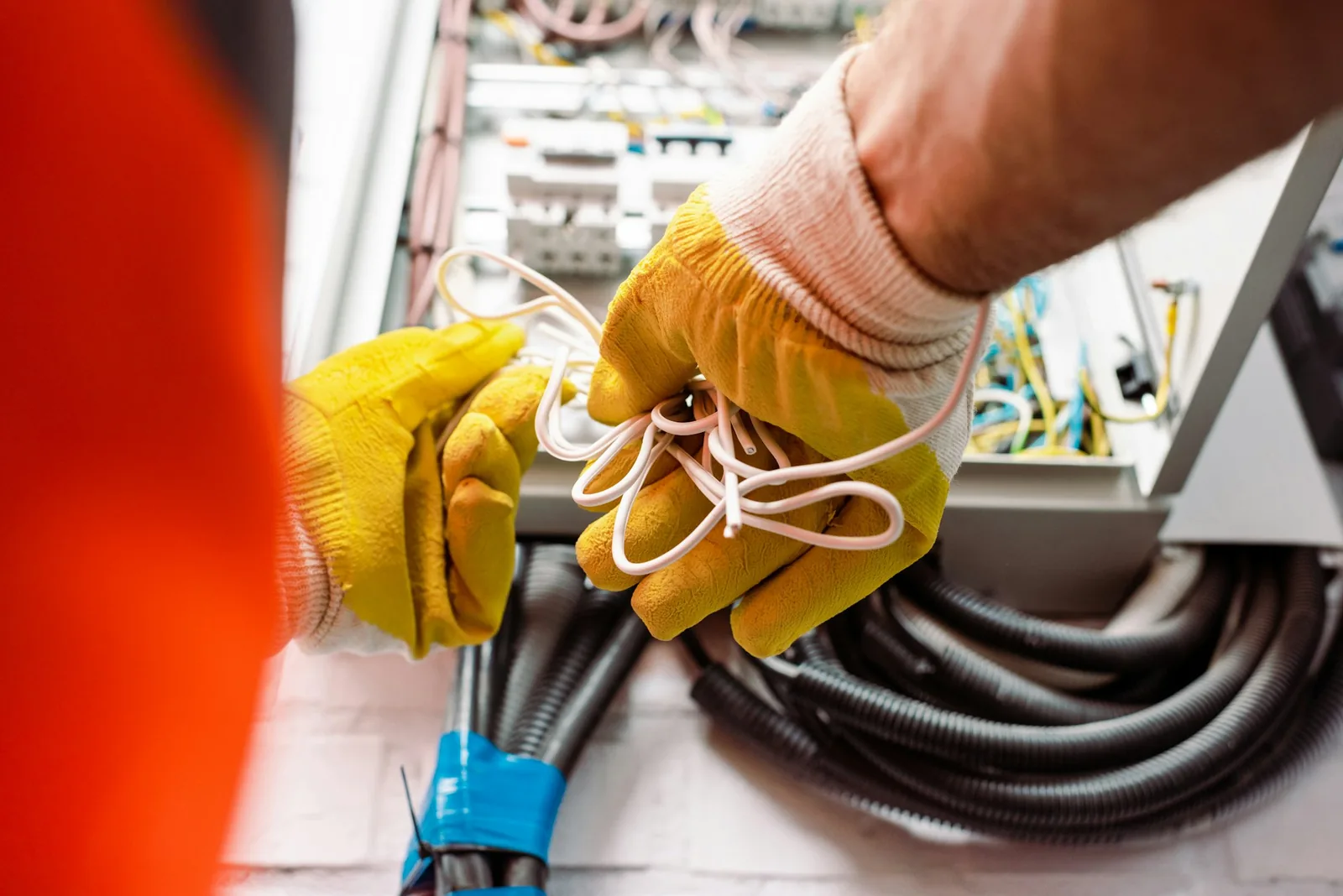 Residential wiring installation - cropped view of electrician in gloves holding wires near electrical bo